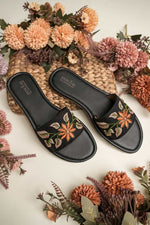 Stepellas black flat sandals featuring a large burnt orange flower hand-embroidery with green leaf accents.