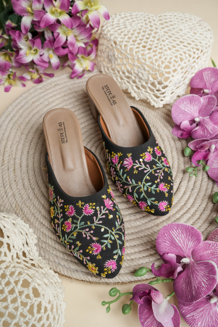 Stepellas black mojdis with white line-art embroidery and colorful leaf motifs.