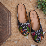 Stepellas black juttis featuring vibrant green, orange, and pink floral embroidery with white vine patterns.