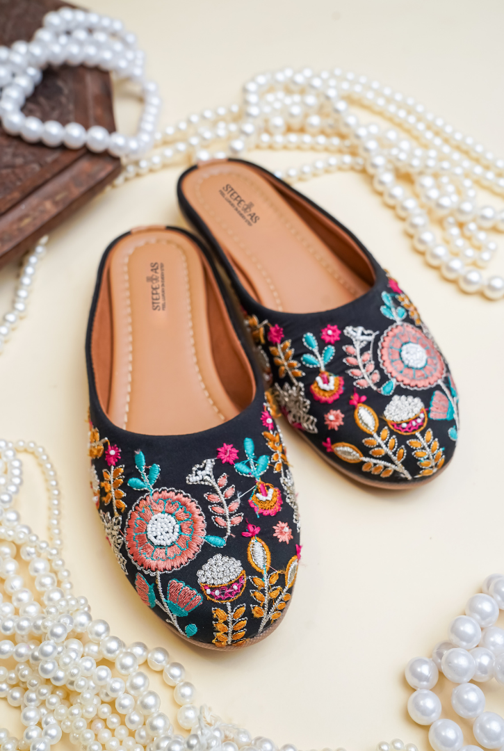 Hand-embroidered Stepellas black mojdis with white line art and colorful orange-green leaf accents.