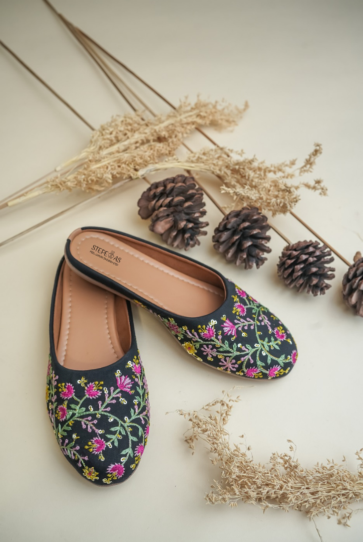 Handcrafted Stepellas black mojdis with white line art embroidery and orange-green leaf accents.