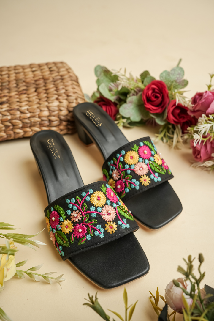 Stepellas black block heels featuring vibrant pink, yellow, and teal floral embroidery with pearl accents.