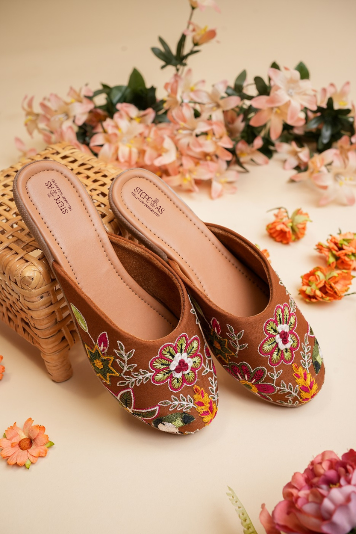 Stepellas coffee color juttis featuring vibrant magenta and green floral embroidery with white accents.