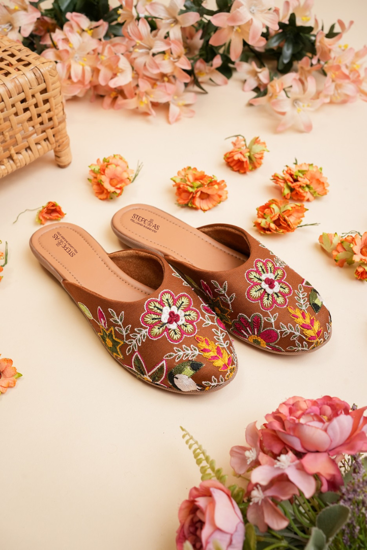 Detailed close-up of the handcrafted multi-color flower and leaf thread work on Stepellas brown juttis.