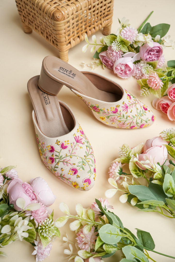 Detailed close-up of the delicate pink floral hand-embroidery and golden sequins on Stepellas cream designer heels.