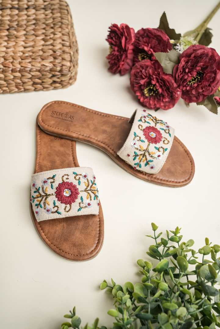 Cream-colored Stepellas flat sandals with a large central maroon floral motif and delicate vine embroidery.