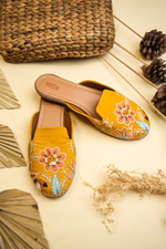 Elegant Stepellas mustard yellow embroidered juttis displayed with rustic palm leaf decor for festive fashion.