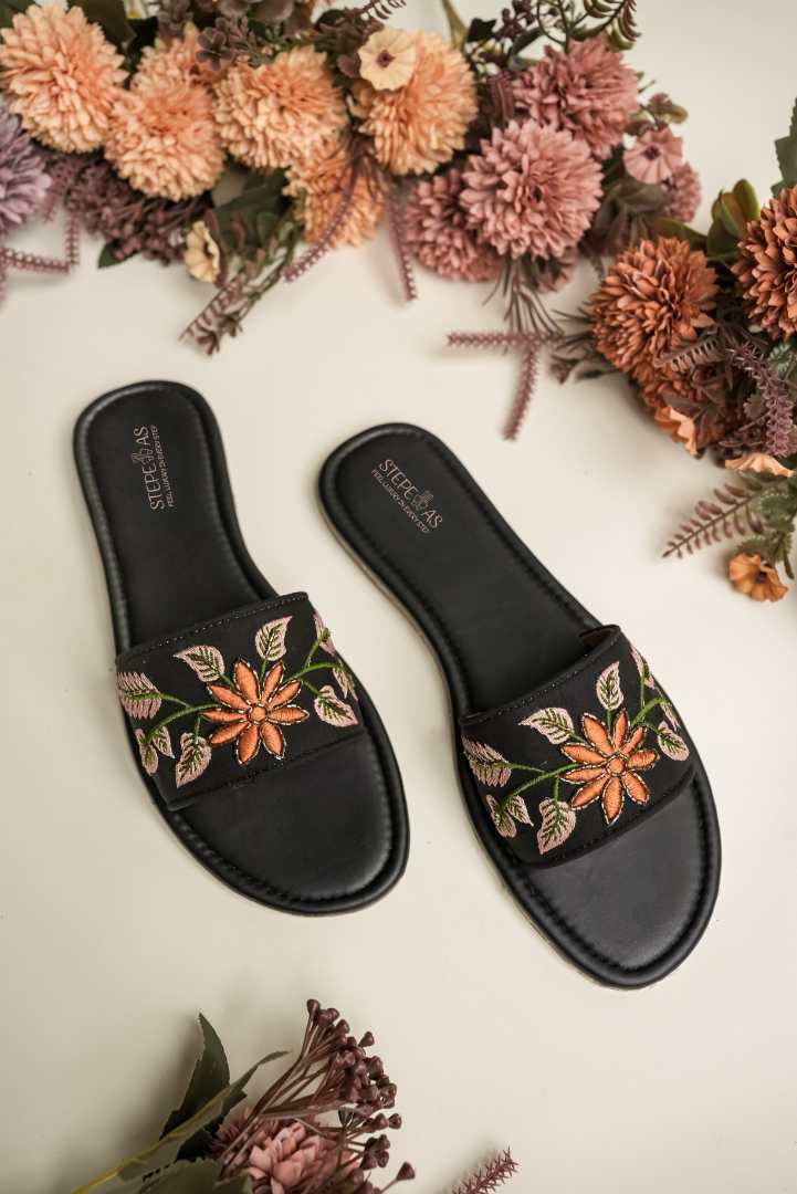 Elegant Stepellas black and orange floral sandals displayed with peach-colored flowers for a festive aesthetic.