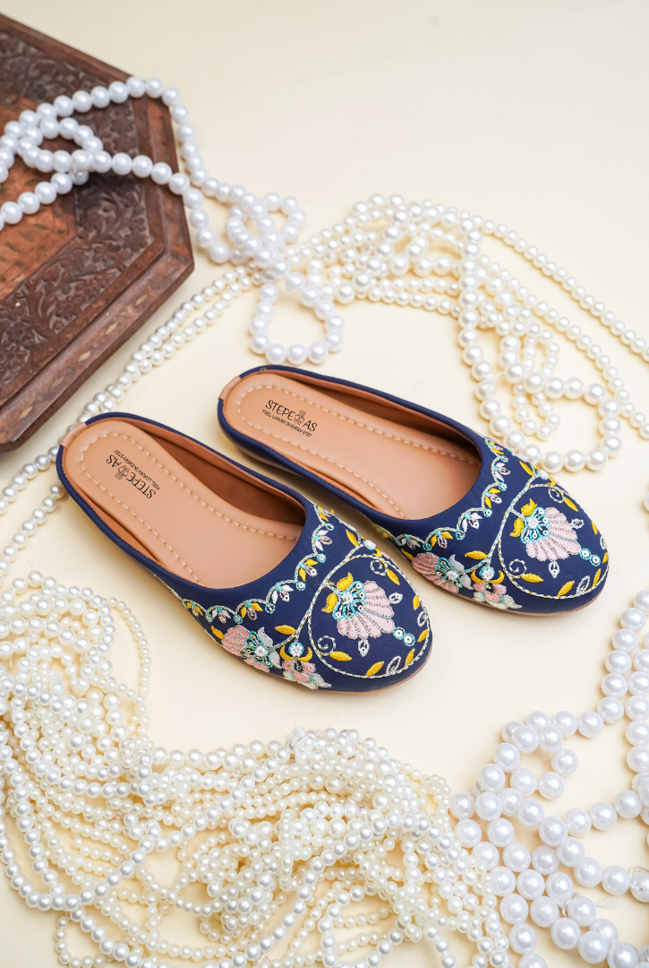 Navy blue embroidered flats with floral patterns on a white surface with pearls and a wooden box.