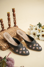 A pair of luxury Stepellas branded black heels with intricate round stone work displayed with aesthetic floral decor.