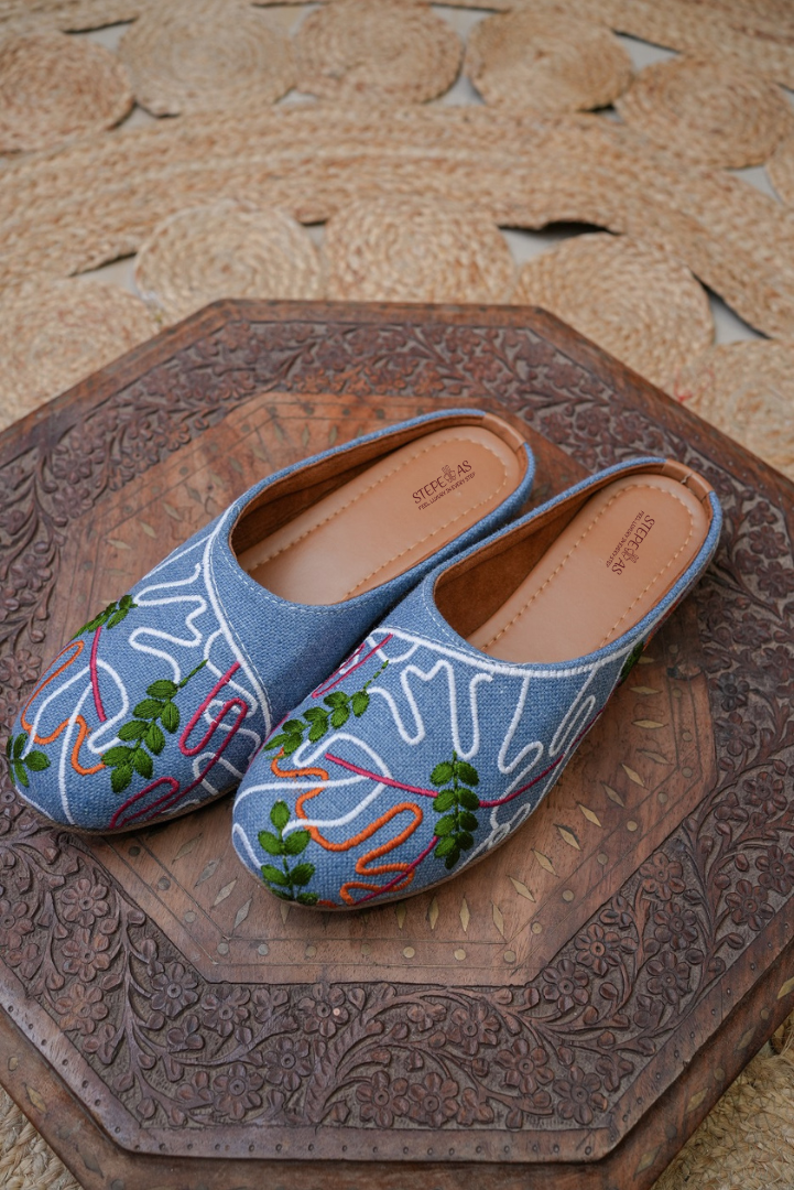Stepellas sky blue denim juttis displayed on a rustic jute rug, highlighting the fusion aesthetic.