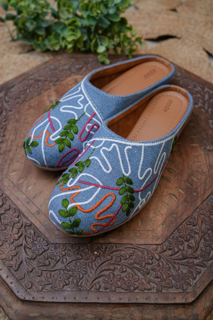 Designer sky blue denim-textured juttis by Stepellas with contemporary white and colorful threadwork.