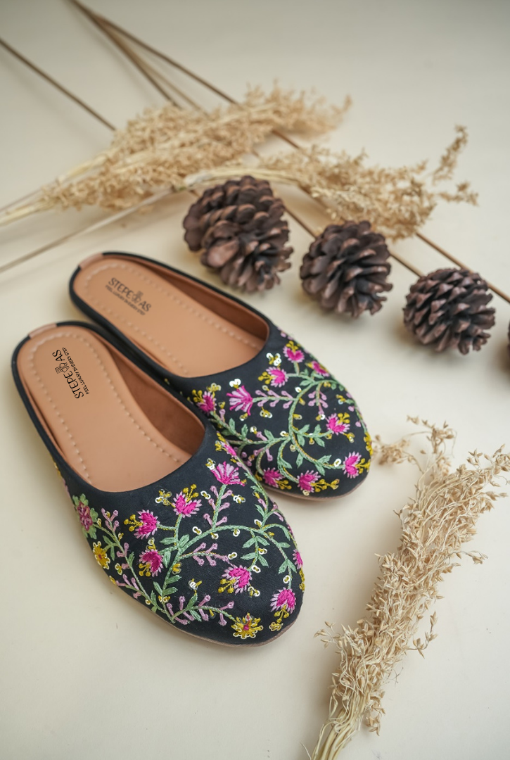 Elegant Stepellas black flower embroidery juttis displayed with rustic autumn-themed decor for festive fashion.