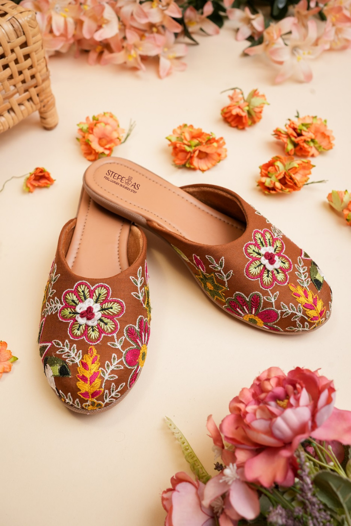 Elegant Stepellas coffee brown embroidered juttis displayed with flowers and a wicker basket for a festive aesthetic.