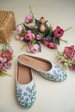 Traditional Stepellas white mojdis with vibrant blue and pink flower threadwork and green leaf details.