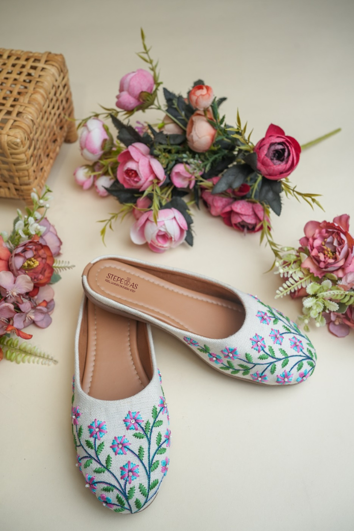 Traditional Stepellas white mojdis with vibrant blue and pink flower threadwork and green leaf details.