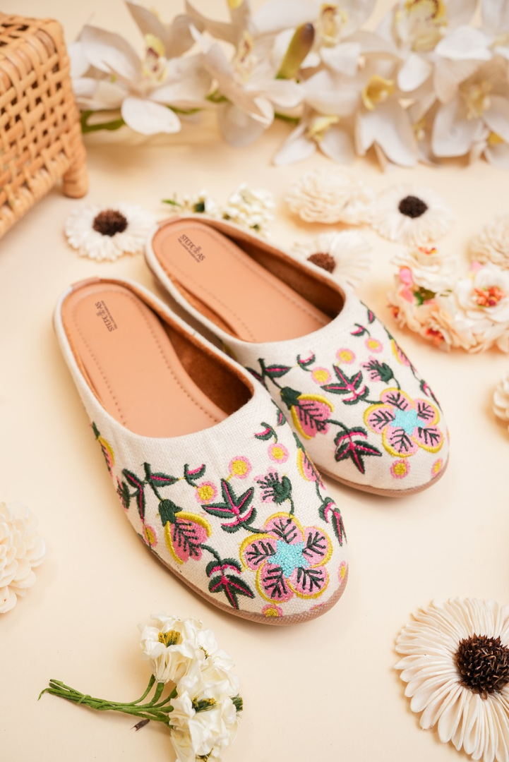 Traditional Stepellas white mojdis with vibrant yellow, pink, and teal floral thread work.