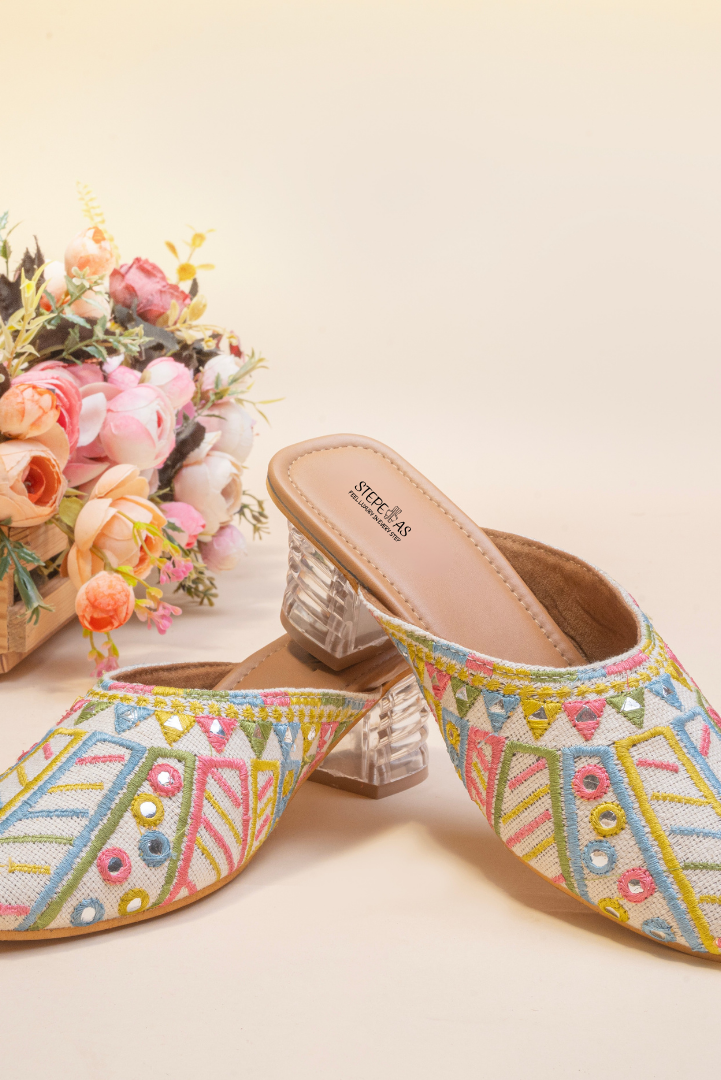 Stepellas white ethnic mules featuring colorful geometric embroidery, foil mirror work, and clear block heels.