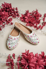 Detailed close-up of the handcrafted pink flowers and shimmering sequin accents on Stepellas white juttis.