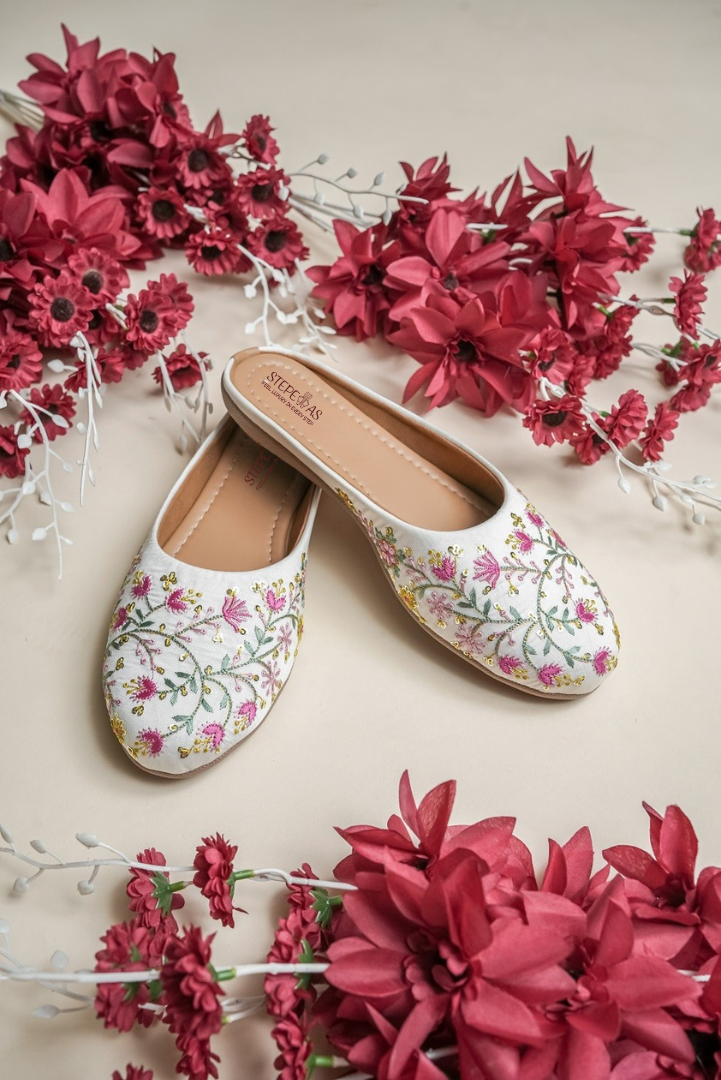 Detailed close-up of the handcrafted pink flowers and shimmering sequin accents on Stepellas white juttis.