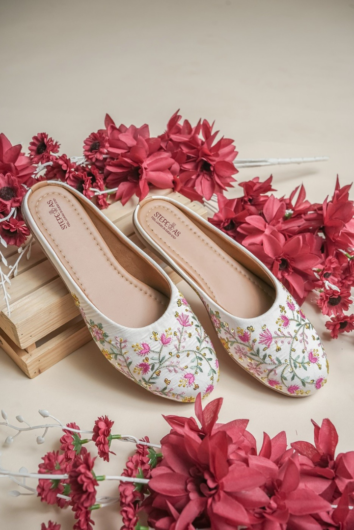 Stepellas white ethnic juttis featuring delicate pink floral embroidery and golden vine threadwork.