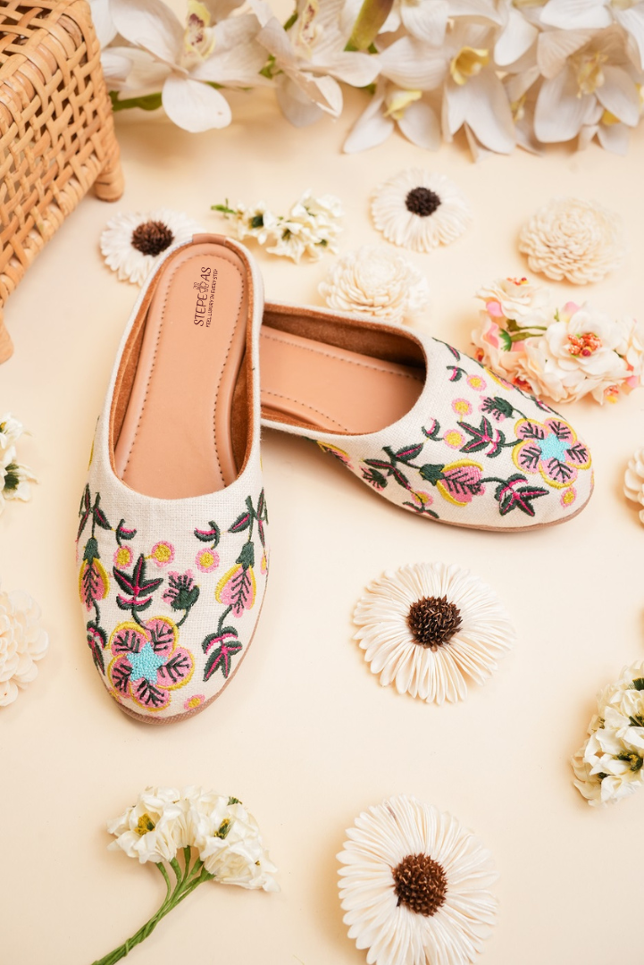 Stepellas white juttis featuring delicate pink floral thread work and shimmering gold sequin accents.